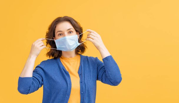 Young woman wearing facemask during coronavirus and flu outbreak. Virus and illness protection, home quarantine. COVID-2019. Taking on or taking off masks. Person on yellow color background. - Foto, Imagem