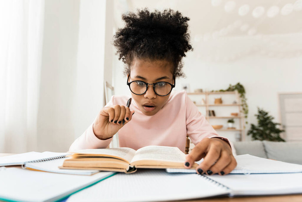 Schockiert African Teen Girl Reading Book Doing Hausaufgaben zu Hause - Foto, Bild
