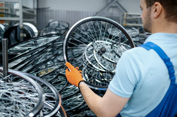 Механік в уніформі тримає велосипедне колесо на заводі. Велосипедні ковзання та збірка спиць у майстерні, установка частин циклу
 - Фото, зображення