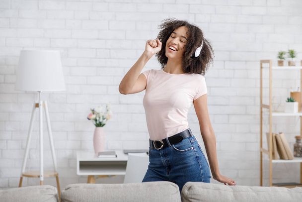 So much fun, stay home alone. African american girl has joy, singing at imaginary microphone and dancing with headphones - Foto, Imagem