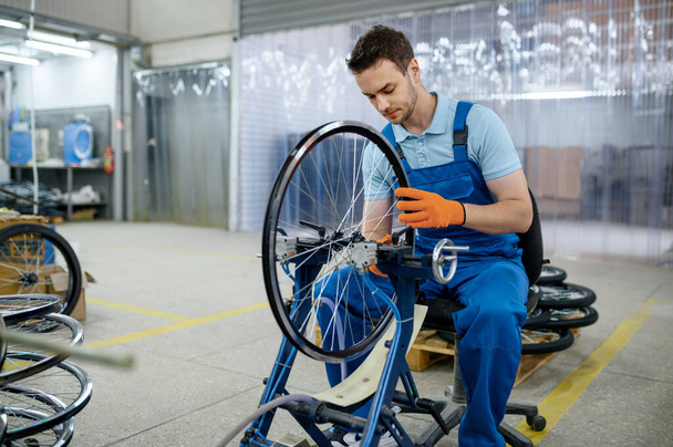 Mannelijke werknemer bij de werktuigmachine controleert fietsvelg op fabriek. Fietswielen gemonteerd in werkplaats - Foto, afbeelding