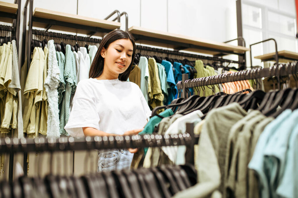 Kobieta wybierająca ubrania w sklepie odzieżowym. Kobieta zakupy w butiku mody, shopper patrząc na odzieży - Zdjęcie, obraz