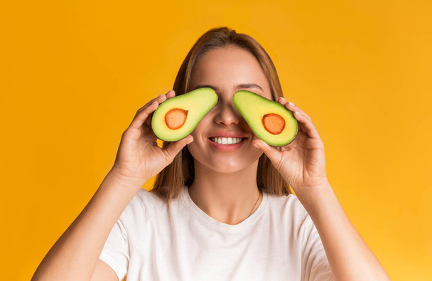 Funny millennial girl covering eyes with two avocado halves and smiling - Fotografie, Obrázek