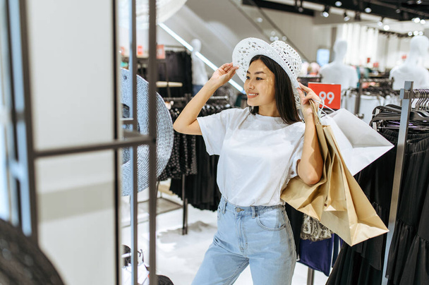 Smiling woman choosing hat in clothing store. Female person shopping in fashion boutique, shopaholic, shopper looking on garment - Foto, afbeelding