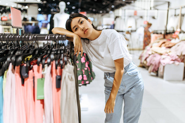 Tired woman at the rack in clothing store. Female person shopping in fashion boutique, shopaholic, shopper looking on garment - Fotografie, Obrázek