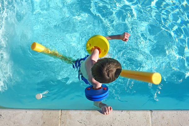 Vista superior del niño flotando en la piscina con flotadores y brazaletes - Foto, Imagen