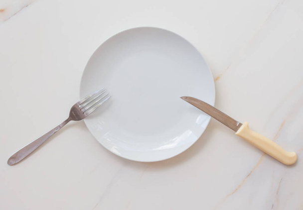  Empty white plate with cutlery on a marble table, saucer, fork and knife. The concept of diet, fasting - Фото, изображение