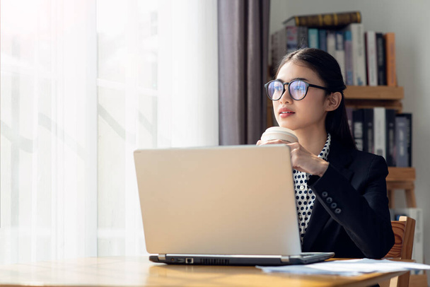 Portrait de jeune femme d'affaires asiatique buvant du café et utilisant son ordinateur portable dans son bureau - Photo, image