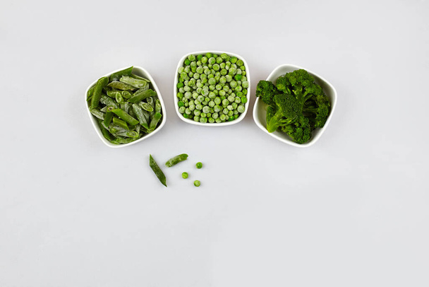 A mix of  frozen  green vegetables: broccoli, string beans and green peas in bowls on a light  grey background. Top view with copy space. - Foto, imagen