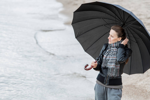 woman with umbrella in winter or autumn walking near sea - Фото, зображення