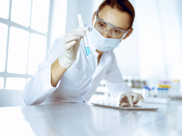 Female laboratory assistant analyzing test tube with blue liquid. Medicine, health care and researching concept - 写真・画像