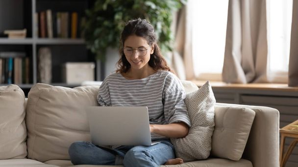 Pretty millennial woman relaxing on couch with computer on laps. - Valokuva, kuva