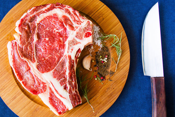 Nyers marhahús az asztalon, fűszerek és rozmaring, Bordaszem steak összetevők. Bors és coars só. Természetes fény. - Fotó, kép