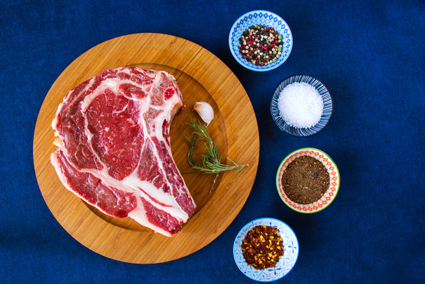 Nyers marhahús az asztalon, fűszerek és rozmaring, Bordaszem steak összetevők. Bors és coars só. Természetes fény. - Fotó, kép