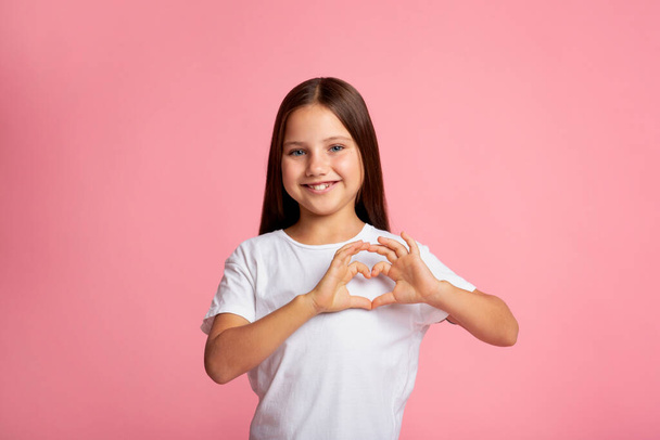 Ausdruck von Gefühlen der Liebe und Güte. Lächelndes kleines Mädchen zeigt Herzzeichen mit Händen - Foto, Bild