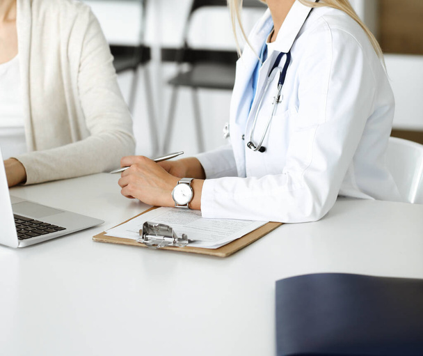 Unknown woman-doctor sitting and communicating with female patient. Physician checks medical history record and exam results, close-up. Healthcare concept - Foto, imagen