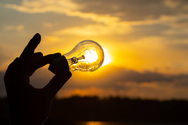 ampoule incandescente à la main sur fond de coucher de soleil fermer - Photo, image