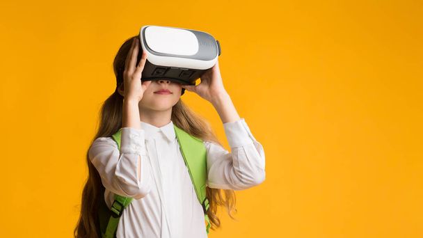 Little Schoolmeisje ervaren virtuele realiteit op gele Studio achtergrond, Panorama - Foto, afbeelding