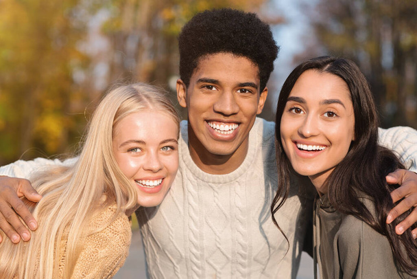 Portrét tří multietnických přátel usmívajících se na pozadí parku - Fotografie, Obrázek