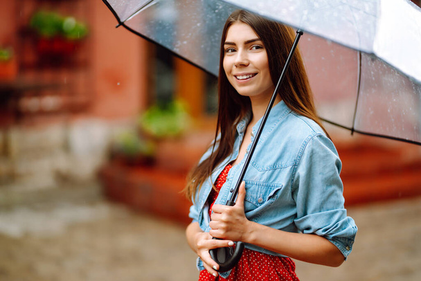 Cheerful woman  under a transparent umbrella enjoying rainfall. Young woman hiding from the rain. Autumn concept. - Photo, image