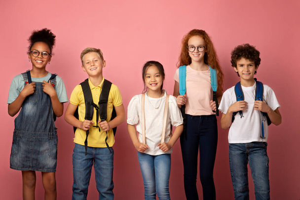 Zpátky do školy. Radostné děti s batohy stojí spolu na růžovém pozadí - Fotografie, Obrázek