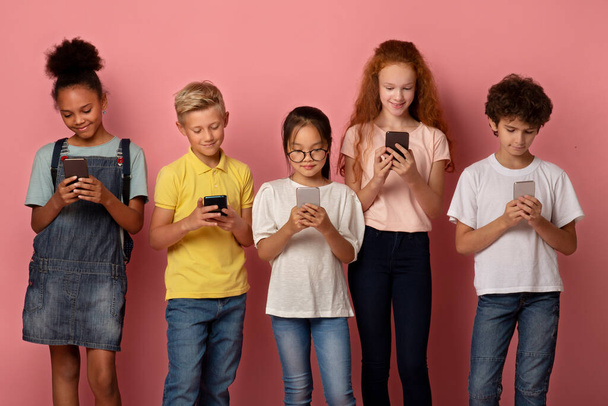 Csoport változatos iskolások ragadt mobiltelefonok tanul online rózsaszín háttér - Fotó, kép