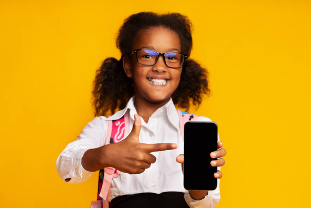 黄色の背景に空白の電話画面を表示するアフリカの女子高生,モックアップ - 写真・画像