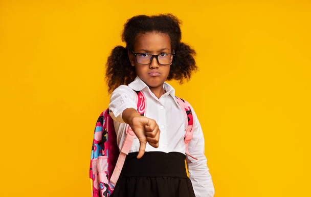 Displeased Black Schoolgirl Gesturing Thumbs-Down Disapproving Something Over Yellow Background - Foto, imagen