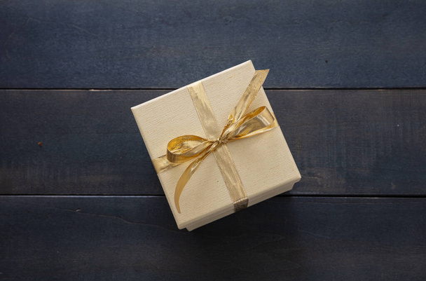 Sorpresa con el concepto actual. Embalaje de caja de regalo cerrada beige con cinta de color oro sobre fondo de mesa de madera azul. vista superior. - Foto, Imagen