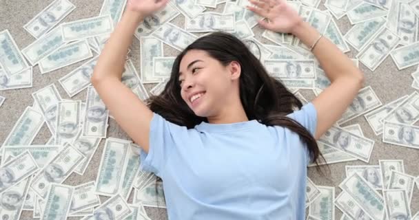 Kobieta leżąca na rozrzuconych banknotach dolarowych - Materiał filmowy, wideo