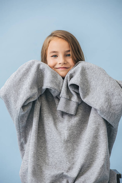 Cute smiling little girl in a huge oversized grey longsleeve over blue - Photo, Image