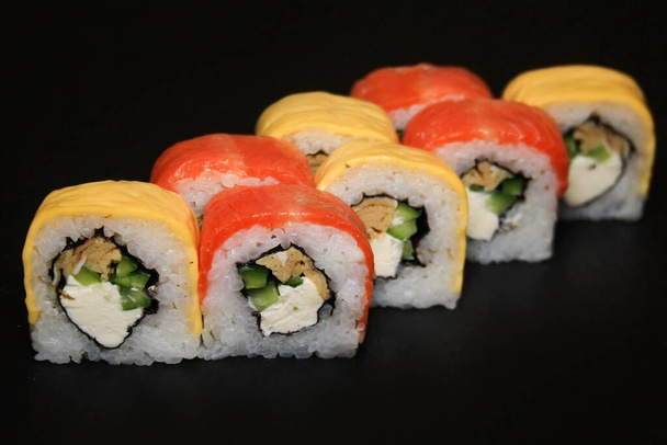 Rouleau de sushi multicolore avec saumon, fromage, concombre et omelette sur fond noir. - Photo, image