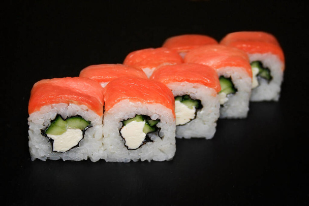 Sushi roll Filadélfia, com creme de queijo, salmão e pepino em um fundo preto. - Foto, Imagem