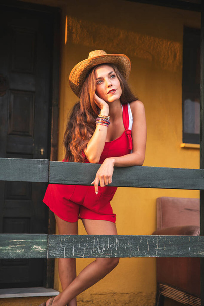 Bella donna con un cappello da cowboy in posa davanti a una fattoria a parete gialla. Fotografia concettuale di moda - Foto, immagini