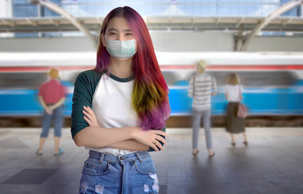 aziatische tiener straat mode met masker en multicolor lang haar en casual met shirt en jeans op de openbare hemel trein in pandemische reizen - Foto, afbeelding