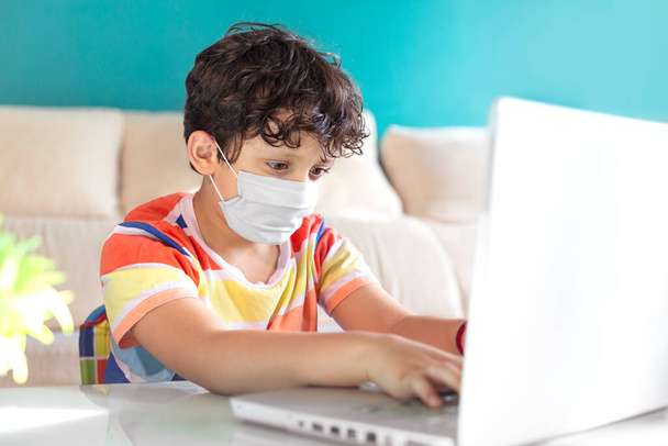 Little boy using a laptop to study from home. He is wearing a face mask. Concept of online education. - Foto, Imagen