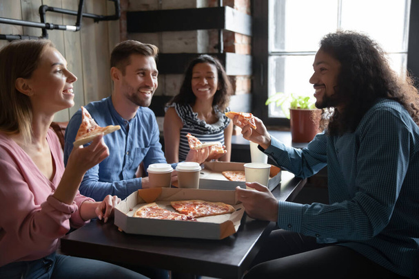Overjoyed diverse friends enjoying pizza in cafe together - Фото, изображение