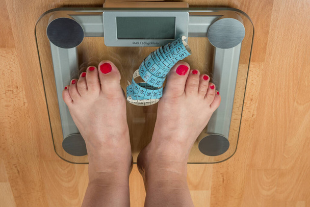 Eine Frau steht mit zwei Füßen auf einer Waage. Übergewichtskonzept - Foto, Bild