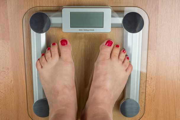Uma mulher está de pé com dois pés em uma balança. Conceito de excesso de peso - Foto, Imagem