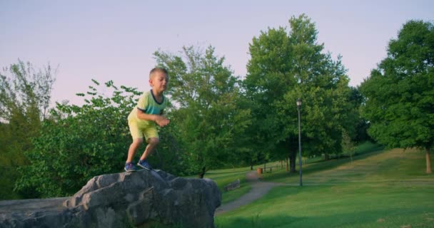 Netter kleiner Junge, der im Sommerpark vom Felsen springt. Rote Kinokamera. Zeitlupe 4k - Filmmaterial, Video