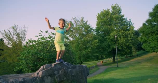 Netter kleiner Junge, der im Sommerpark vom Felsen springt. Rote Kinokamera. Zeitlupe 4k - Filmmaterial, Video