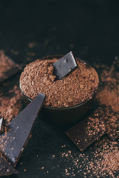 Pièces de barre de chocolat avec poudre de cacao sur fond sombre, espace pour faire face. - Photo, image