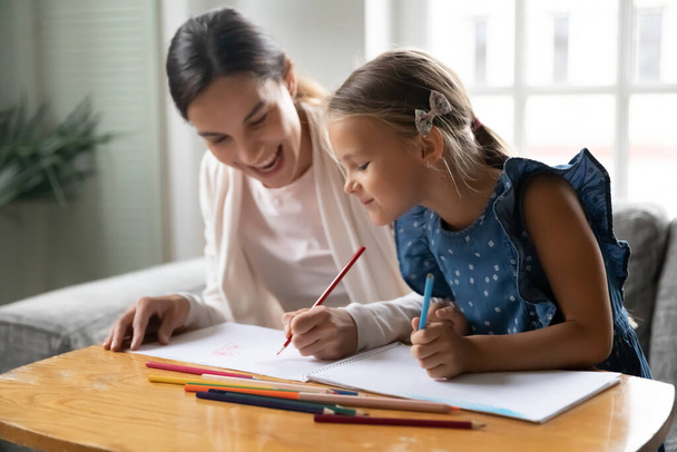 Smiling millennial mother enjoying drawing pictures with small child girl. - Foto, immagini