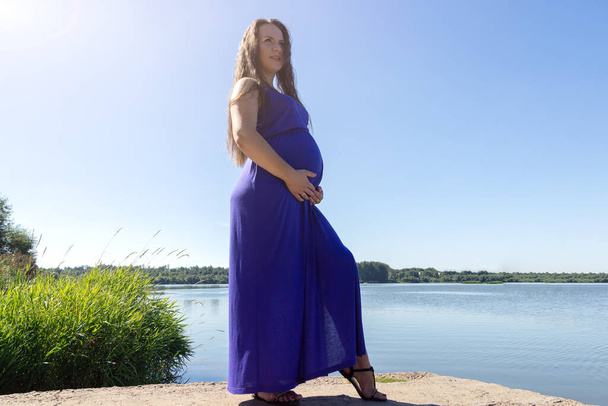 Beautiful pregnant woman in blue dress feeling lovely and Relax in the beach with warm light - Foto, Imagem