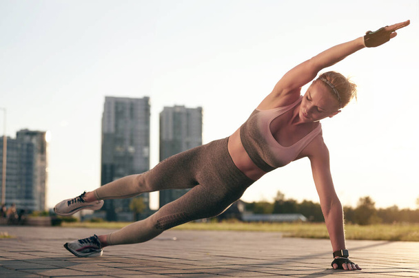 Sivulankku kuntoilu. Urheilullinen nainen treenaa ulkona auringonlaskun aikaan. Käsite urheilu, virkistys ja motivaatio. Laadukas kuva - Valokuva, kuva