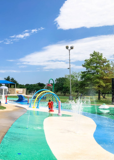 Colorful splash pad water playground with Asian toddler boy playing near Dallas, Texas, America - Photo, Image