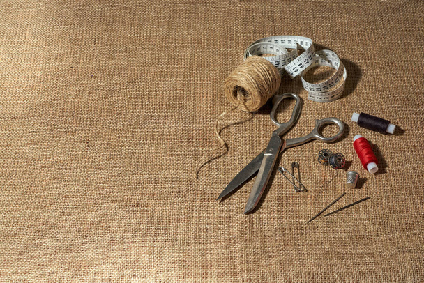 Outils faits à la main : dé à coudre, fil, aiguille, broche, ruban à mesurer, ciseaux sur fond brun - Photo, image