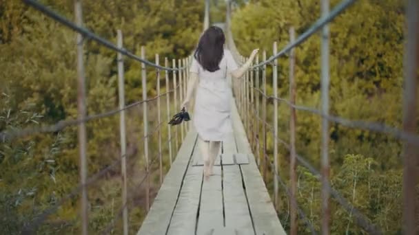 Egy gyönyörű ruhás nő, aki egy hídon fut az erdőben. - Felvétel, videó
