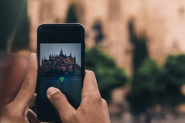 utilizzare il telefono cellulare per scattare una foto di un ragazzo con la cattedrale di Segovia in Spagna come sfondo in una giornata estiva - Foto, immagini