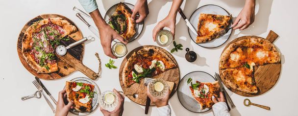 Pizza party for friends or family. Flat-lay of various pizzas, drinks and people celebrating over plain white table background, top view. Fast food, comfort food, Italian cuisine concept - 写真・画像